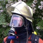 PA-Träger mit angelegter Dräger Panorama-Nova-Maske mit Einheitssteckanschluß (erkennbar an der roten Abdeckkappe) und angelegter Flammschutzhaube