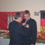 Wehrführer Thomsen Stern bringt an Reinhards Uniform das Abzeichen für 25 Jahre FF-Zugehörigkeit an.